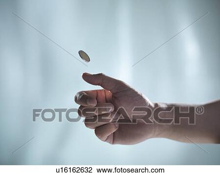 Stock Image - Close up of hand tossing coin. Fotosearch