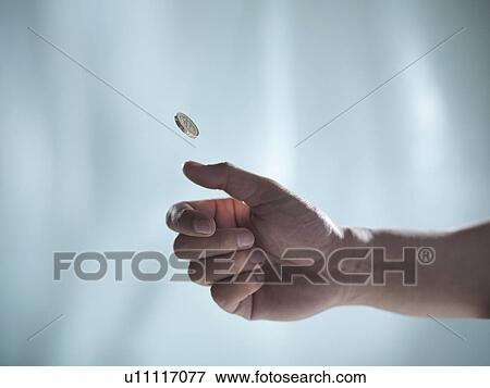 Stock Photo - Close up of hand tossing coin. Fotosearch
