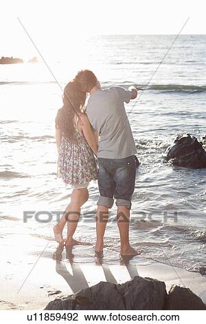 Stock Image - Couple admiring ocean on beach. Fotosearch