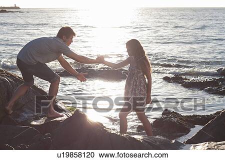 Stock Image - Couple climbing rocks on beach. Fotosearch
