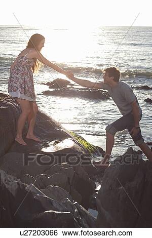 Couple climbing rocks on beach View Large Photo Image Stock Photograph - Couple climbing rocks on beach. Fotosearch