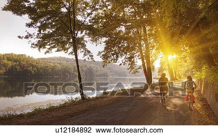 Couple riding bicycles by river bank View Large Photo Image Stock Image - Couple riding bicycles by river bank. Fotosearch