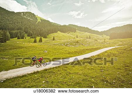 Stock Image - Couple riding bicycles on rural road. Fotosearch