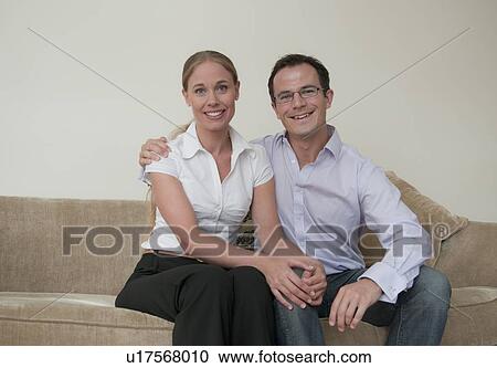 Couple sitting on sofa together View Large Photo Image Stock Image - Couple sitting on sofa together. Fotosearch