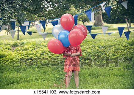 Stock Image - Girl holding bunch of balloons outdoors. Fotosearch