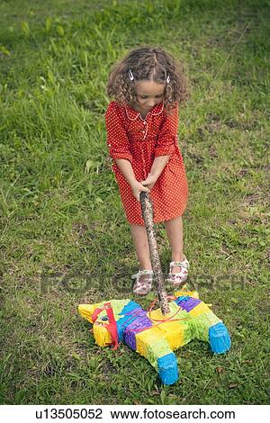 Stock Image - Girl opening pinata on ground at party. Fotosearch