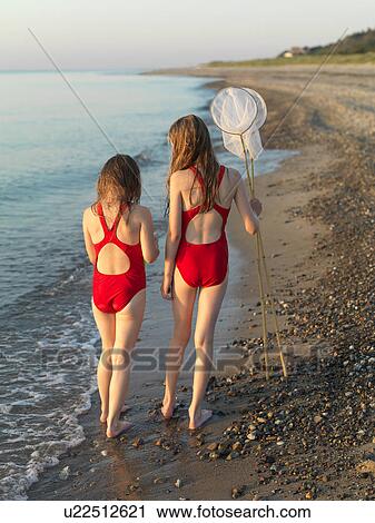 Stock Image - Girls walking on rocky beach. Fotosearch