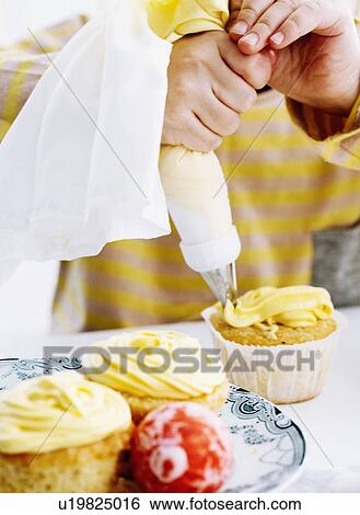 Hands icing cupcake on table View Large Photo Image Stock Photograph - Hands icing cupcake on table. Fotosearch