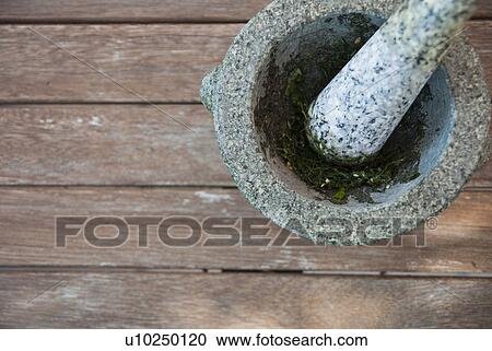 Stock Image - Herbs being ground in pestle and mortar. Fotosearch