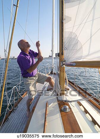 Stock Photography - Man adjusting rigging on sailboat. Fotosearch