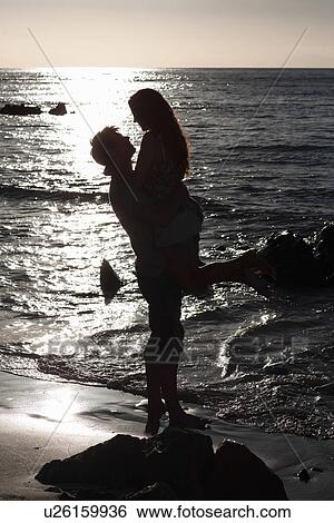 Stock Photograph - Man lifting girlfriend on beach. Fotosearch