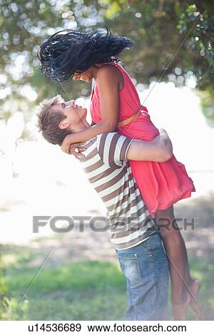Stock Photo - Man lifting girlfriend outdoors. Fotosearch