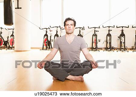 Stock Image - Man meditating on mat at gym. Fotosearch