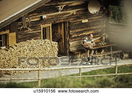 Stock Photograph - Man reading in porch of log cabin. Fotosearch