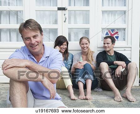 Stock Image - Man sitting with family outside house. Fotosearch
