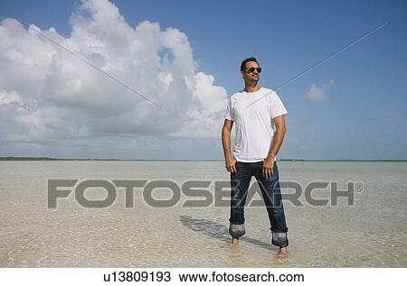 Man standing in water on tropical beach View Large Photo Image Stock Image - Man standing in water on tropical beach. Fotosearch