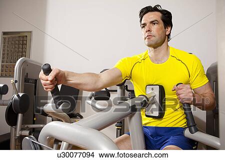 Picture - Man using exercise equipment at gym. Fotosearch