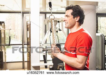 Stock Image - Man using exercise equipment at gym. Fotosearch