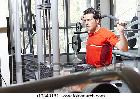 Stock Image - Man using exercise equipment at gym. Fotosearch