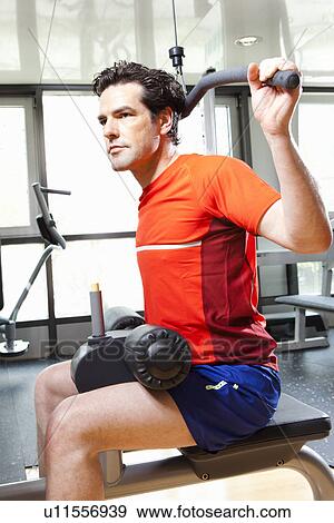 Stock Photo - Man using exercise equipment at gym. Fotosearch