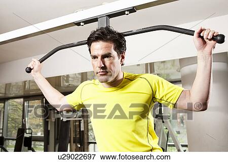Stock Photo - Man using exercise equipment at gym. Fotosearch
