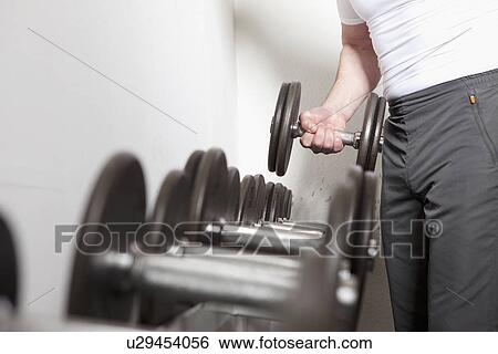 Stock Photograph - Man using free weights at gym. Fotosearch