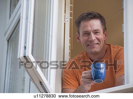 Stock Image - Man with coffee leaning out window. Fotosearch