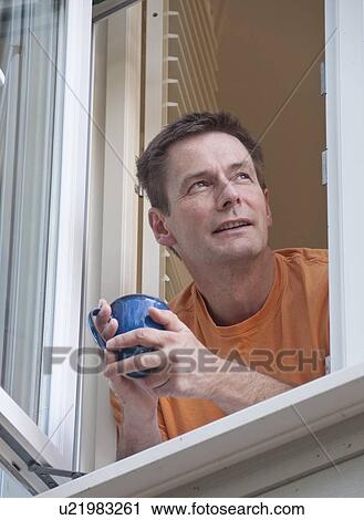 Man with coffee leaning out window View Large Photo Image Stock Image - Man with coffee leaning out window. Fotosearch