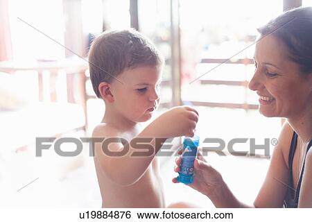 Stock Photograph - Mother and son blowing bubbles indoors. Fotosearch