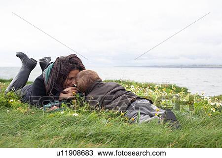 Stock Image - Mother and son laying in grassy field. Fotosearch