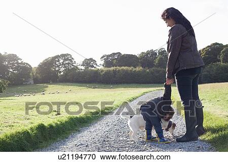 Stock Image - Mother and son walking dog on dirt road. Fotosearch