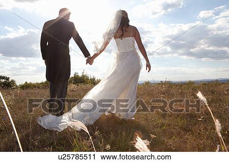 Stock Image - Newlywed couple holding hands in grass. Fotosearch