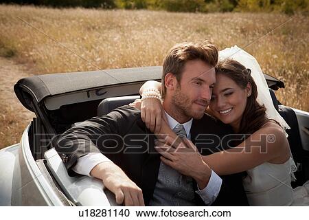 Stock Image - Newlywed couple hugging in convertible. Fotosearch