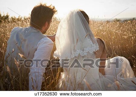Stock Image - Newlywed couple sitting in tall grass. Fotosearch