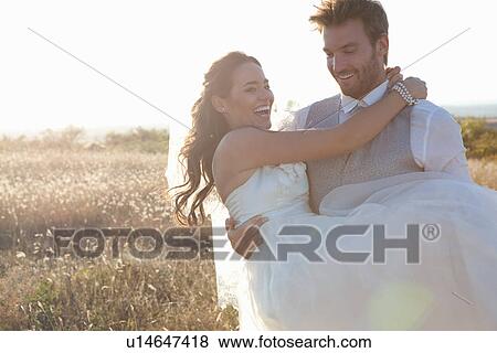 Newlywed groom carrying bride outdoors View Large Photo Image Stock Photo - Newlywed groom carrying bride outdoors. Fotosearch