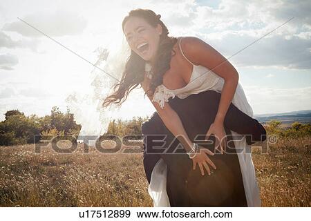 Stock Photo - Newlywed groom carrying bride outdoors. Fotosearch