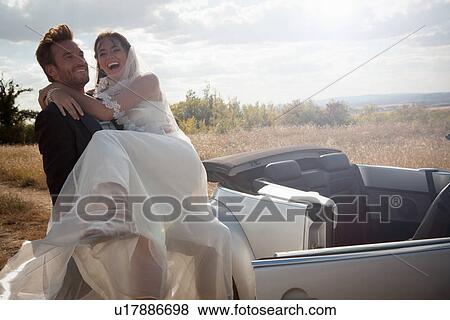 Stock Photo - Newlywed groom carrying bride outdoors. Fotosearch