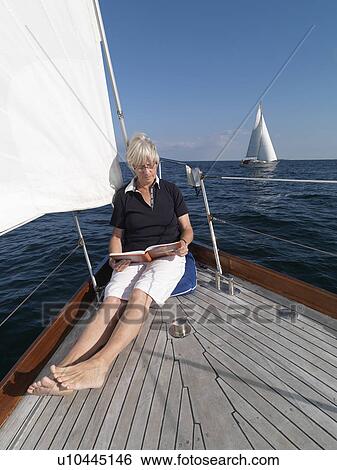 Stock Photograph - Older woman reading on sailboat. Fotosearch