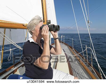 Picture - Older woman using binoculars on sailboat. Fotosearch