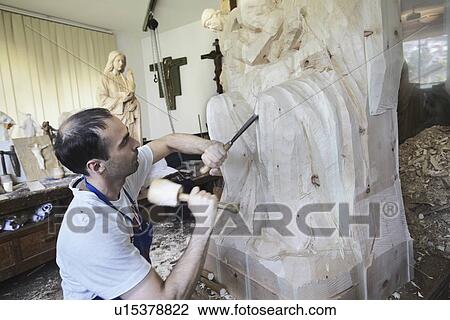 Stock Image - Sculptor chiseling figure from wood. Fotosearch