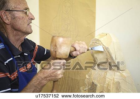 Stock Image - Sculptor chiseling figure from wood. Fotosearch