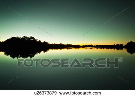 Sky and trees reflected in still lake View Large Photo Image Stock Photo - Sky and trees reflected in still lake. Fotosearch