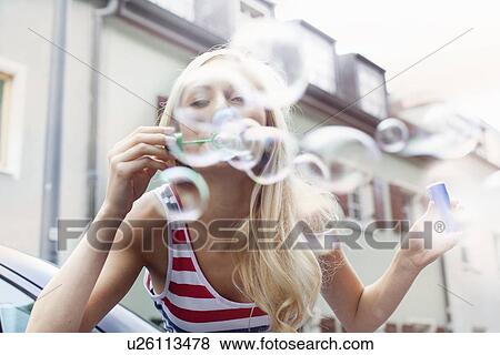 Stock Photo - Smiling woman blowing bubbles outdoors. Fotosearch