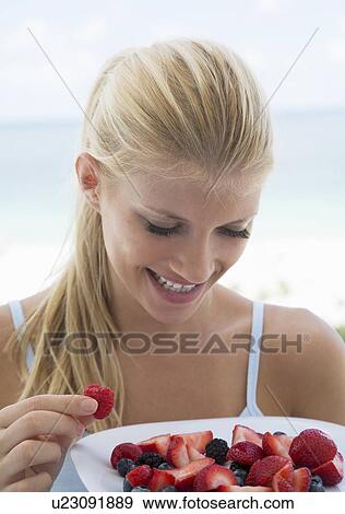 Smiling woman eating plate of fruit View Large Photo Image Stock Photo - Smiling woman eating plate of fruit. Fotosearch