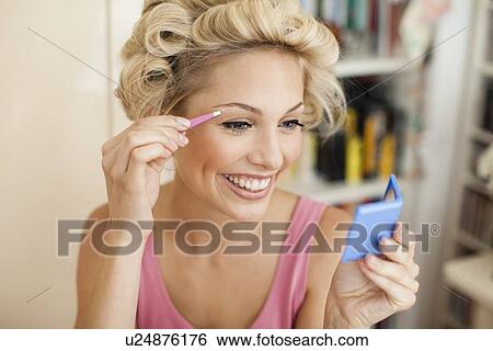 Stock Photograph - Smiling woman plucking her eyebrows. Fotosearch