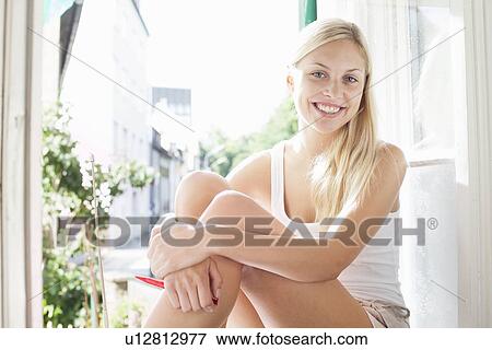 Stock Photo - Smiling woman sitting in windowsill. Fotosearch