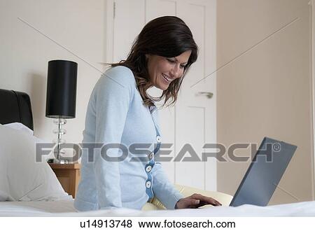Stock Photo - Smiling woman using laptop in bed. Fotosearch