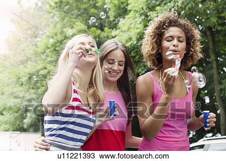 Stock Image - Smiling women blowing bubbles outdoors. Fotosearch