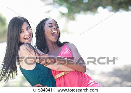 Stock Image - Smiling women hugging outdoors. Fotosearch