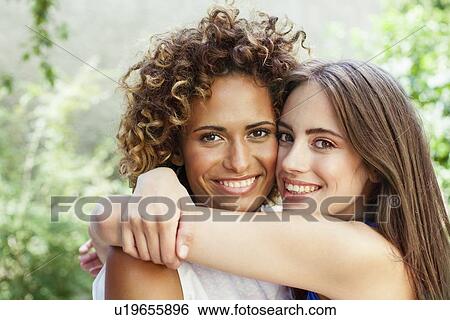 Stock Photograph - Smiling women hugging outdoors. Fotosearch